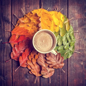 Coffee cup on the autumn leaves and old wooden table background. Top view with copy space