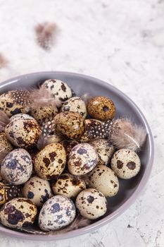 pile of Easter quail eggs on gray fabric cotton rag on concrete background, Round ceramic plate. Space for text