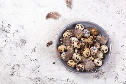 pile of Easter quail eggs on gray fabric cotton rag on concrete background, Round ceramic plate. Space for text