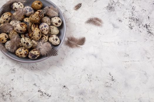 pile of Easter quail eggs on gray fabric cotton rag on concrete background, Round ceramic plate. Space for text