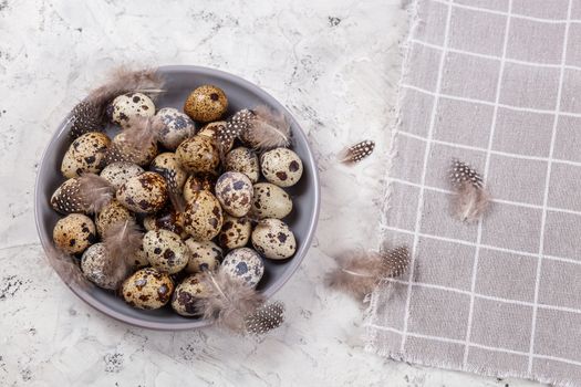 pile of Easter quail eggs on gray fabric cotton rag on concrete background, Round ceramic plate. Space for text