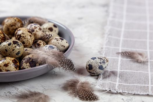 pile of Easter quail eggs on gray fabric cotton rag on concrete background, Round ceramic plate. Space for text