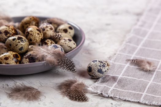 pile of Easter quail eggs on gray fabric cotton rag on concrete background, Round ceramic plate. Space for text