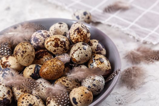 pile of Easter quail eggs on gray fabric cotton rag on concrete background, Round ceramic plate. Space for text