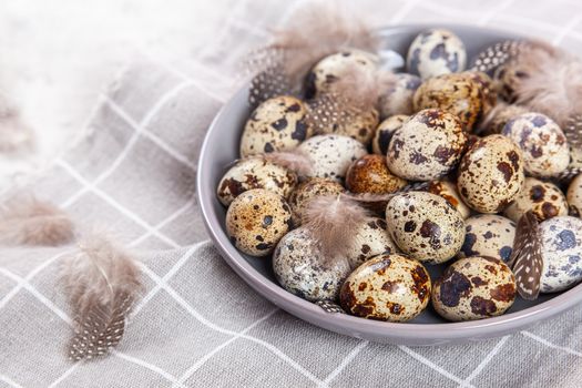 pile of Easter quail eggs on gray fabric cotton rag on concrete background, Round ceramic plate. Space for text