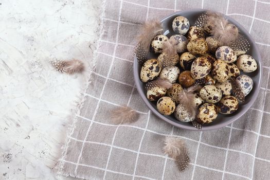 pile of Easter quail eggs on gray fabric cotton rag on concrete background, Round ceramic plate. Space for text
