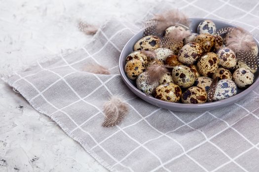 pile of Easter quail eggs on gray fabric cotton rag on concrete background, Round ceramic plate. Space for text