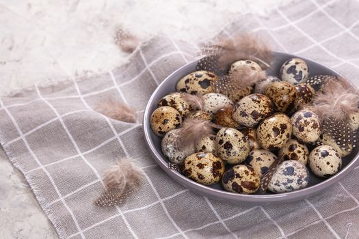 pile of Easter quail eggs on gray fabric cotton rag on concrete background, Round ceramic plate. Space for text