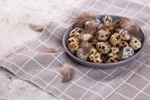 pile of Easter quail eggs on gray fabric cotton rag on concrete background, Round ceramic plate. Space for text