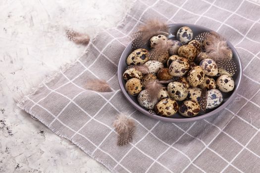 pile of Easter quail eggs on gray fabric cotton rag on concrete background, Round ceramic plate. Space for text