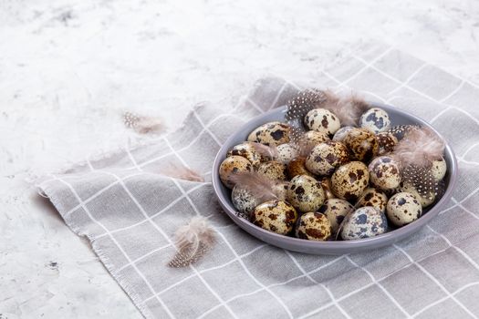 pile of Easter quail eggs on gray fabric cotton rag on concrete background, Round ceramic plate. Space for text