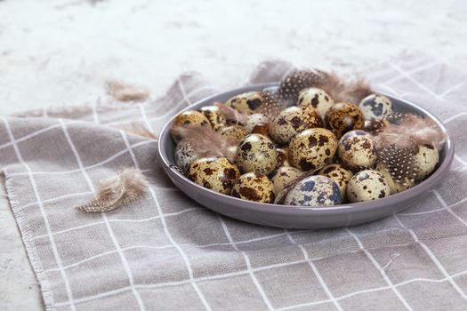 pile of Easter quail eggs on gray fabric cotton rag on concrete background, Round ceramic plate. Space for text