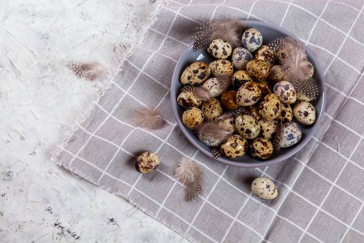 pile of Easter quail eggs on gray fabric cotton rag on concrete background, Round ceramic plate. Space for text