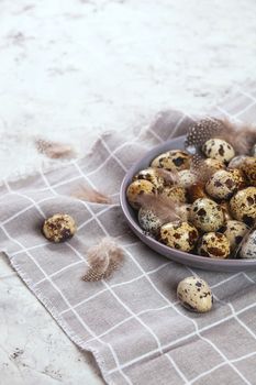 pile of Easter quail eggs on gray fabric cotton rag on concrete background, Round ceramic plate. Space for text