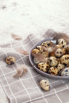 pile of Easter quail eggs on gray fabric cotton rag on concrete background, Round ceramic plate. Space for text