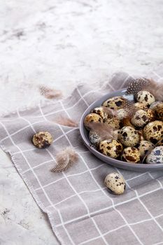pile of Easter quail eggs on gray fabric cotton rag on concrete background, Round ceramic plate. Space for text