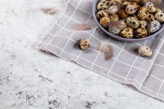pile of Easter quail eggs on gray fabric cotton rag on concrete background, Round ceramic plate. Space for text