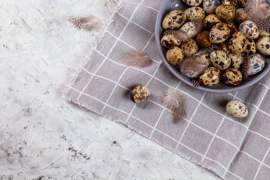 pile of Easter quail eggs on gray fabric cotton rag on concrete background, Round ceramic plate. Space for text