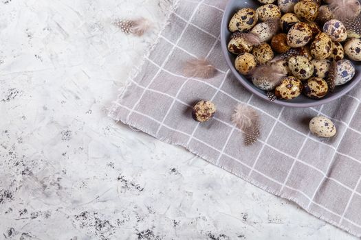 pile of Easter quail eggs on gray fabric cotton rag on concrete background, Round ceramic plate. Space for text