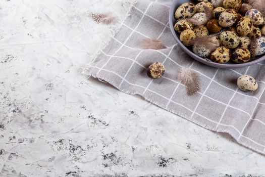 pile of Easter quail eggs on gray fabric cotton rag on concrete background, Round ceramic plate. Space for text