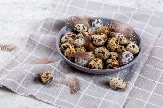 pile of Easter quail eggs on gray fabric cotton rag on concrete background, Round ceramic plate. Space for text
