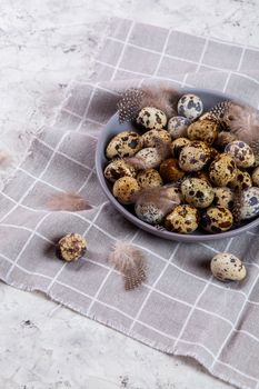 pile of Easter quail eggs on gray fabric cotton rag on concrete background, Round ceramic plate. Space for text