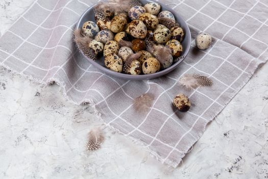 pile of Easter quail eggs on gray fabric cotton rag on concrete background, Round ceramic plate. Space for text