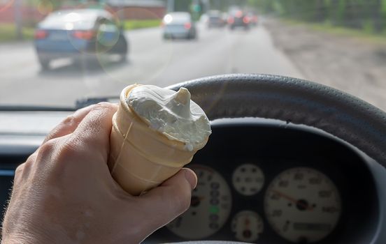 ice cream in the hand of the driver of the car against the background of the roadway with moving traffic