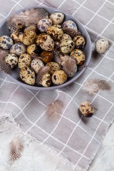 pile of Easter quail eggs on gray fabric cotton rag on concrete background, Round ceramic plate. Space for text