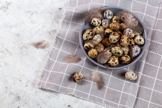 pile of Easter quail eggs on gray fabric cotton rag on concrete background, Round ceramic plate. Space for text