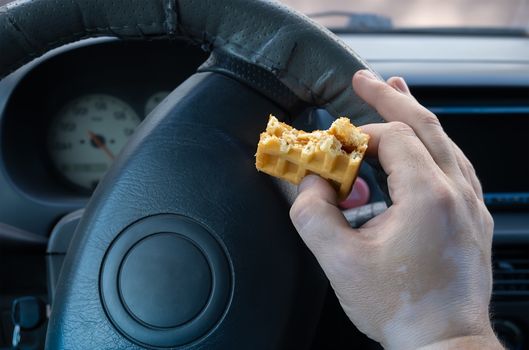fast food, cookies, snack for lunch in the hand of the driver of the car on the background of the steering wheel