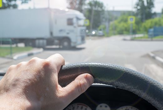 view of the driver hand at the wheel of a car at a road intersection that gives way to a cargo van passing by
