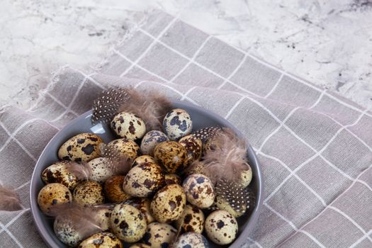 pile of Easter quail eggs on gray fabric cotton rag on concrete background, Round ceramic plate. Space for text