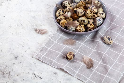 pile of Easter quail eggs on gray fabric cotton rag on concrete background, Round ceramic plate. Space for text