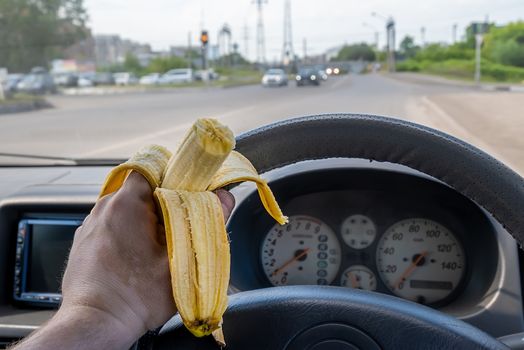 food, a banana in the driver hand while driving at the wheel of a car passing on the road