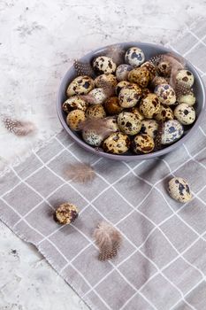 pile of Easter quail eggs on gray fabric cotton rag on concrete background, Round ceramic plate. Space for text