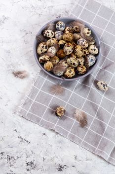pile of Easter quail eggs on gray fabric cotton rag on concrete background, Round ceramic plate. Space for text
