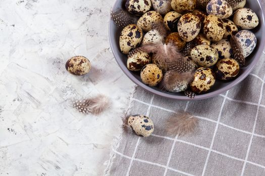pile of Easter quail eggs on gray fabric cotton rag on concrete background, Round ceramic plate. Space for text