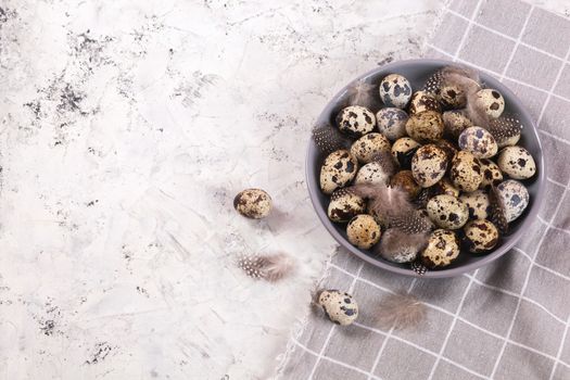 pile of Easter quail eggs on gray fabric cotton rag on concrete background, Round ceramic plate. Space for text