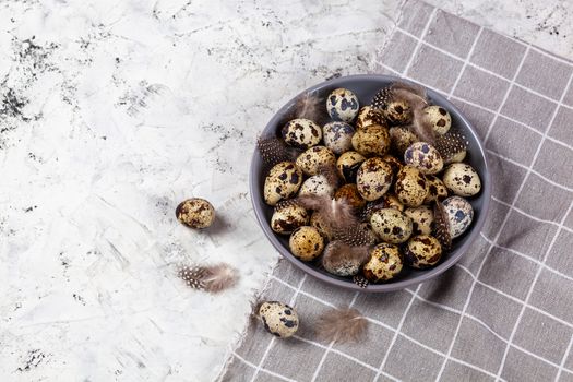 pile of Easter quail eggs on gray fabric cotton rag on concrete background, Round ceramic plate. Space for text