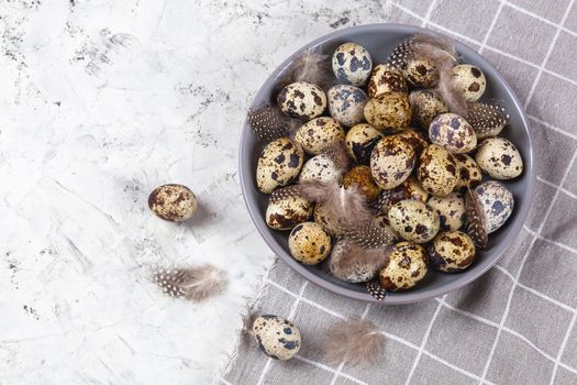 pile of Easter quail eggs on gray fabric cotton rag on concrete background, Round ceramic plate. Space for text