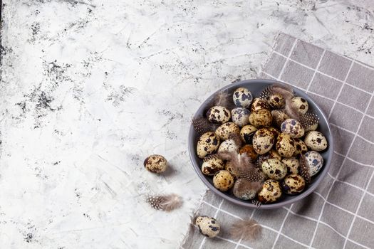 pile of Easter quail eggs on gray fabric cotton rag on concrete background, Round ceramic plate. Space for text