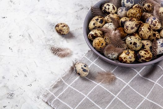 pile of Easter quail eggs on gray fabric cotton rag on concrete background, Round ceramic plate. Space for text