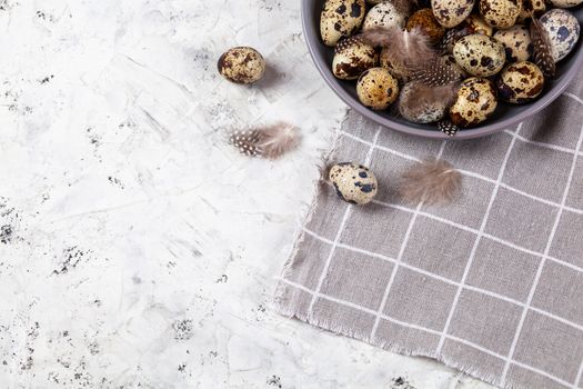 pile of Easter quail eggs on gray fabric cotton rag on concrete background, Round ceramic plate. Space for text
