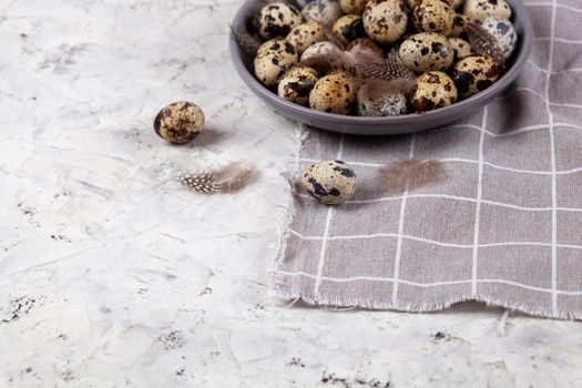 pile of Easter quail eggs on gray fabric cotton rag on concrete background, Round ceramic plate. Space for text