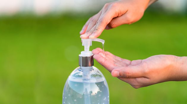 Closeup Asian woman hand using wash hand sanitizer gel pump dispenser before work over photo blurred of green color of grass while Coronavirus Network Outbreak, health care and covid19 concept