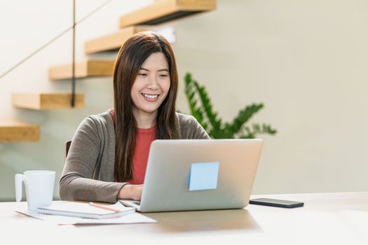 Asian business woman using technology laptop and mobile phone for work from home in indoor modern house, freelance and entrepreneur,startups and business owner, social distance and self responsibility