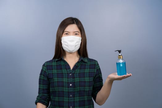 Portrait of asian female wearing face surgical mask and presenting alcohol gel or hand sanitizer on blue color background, covid19 outbreak and pandemic,healthcare and protection against virus concept