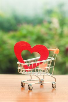 Red wooden heart in the trading cart. concept of buying love. nature background. Health care and purchase of medicines. Health care budget. Love for shopping. Favorite store. Buy love and happiness.