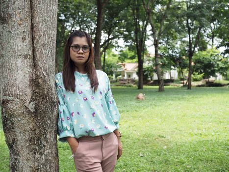 Portrait of an Asian woman standing next to a tree in the park The background is a green tree.